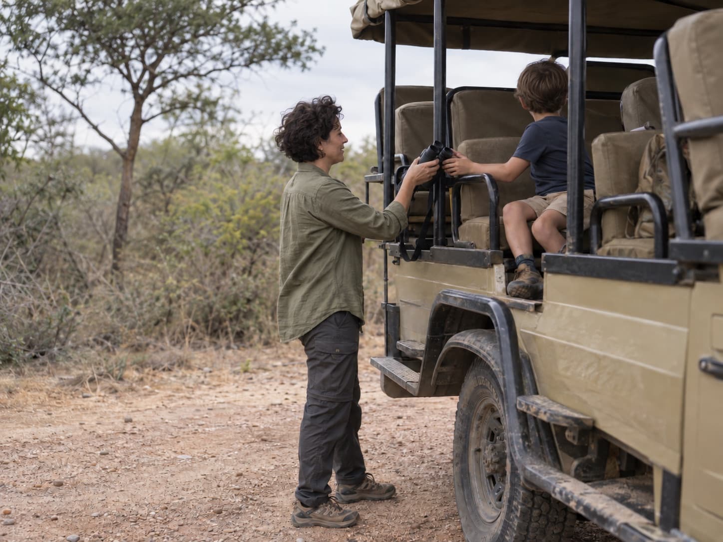 A mother handing binoculars to her son on a safari vehicle in Madikwe